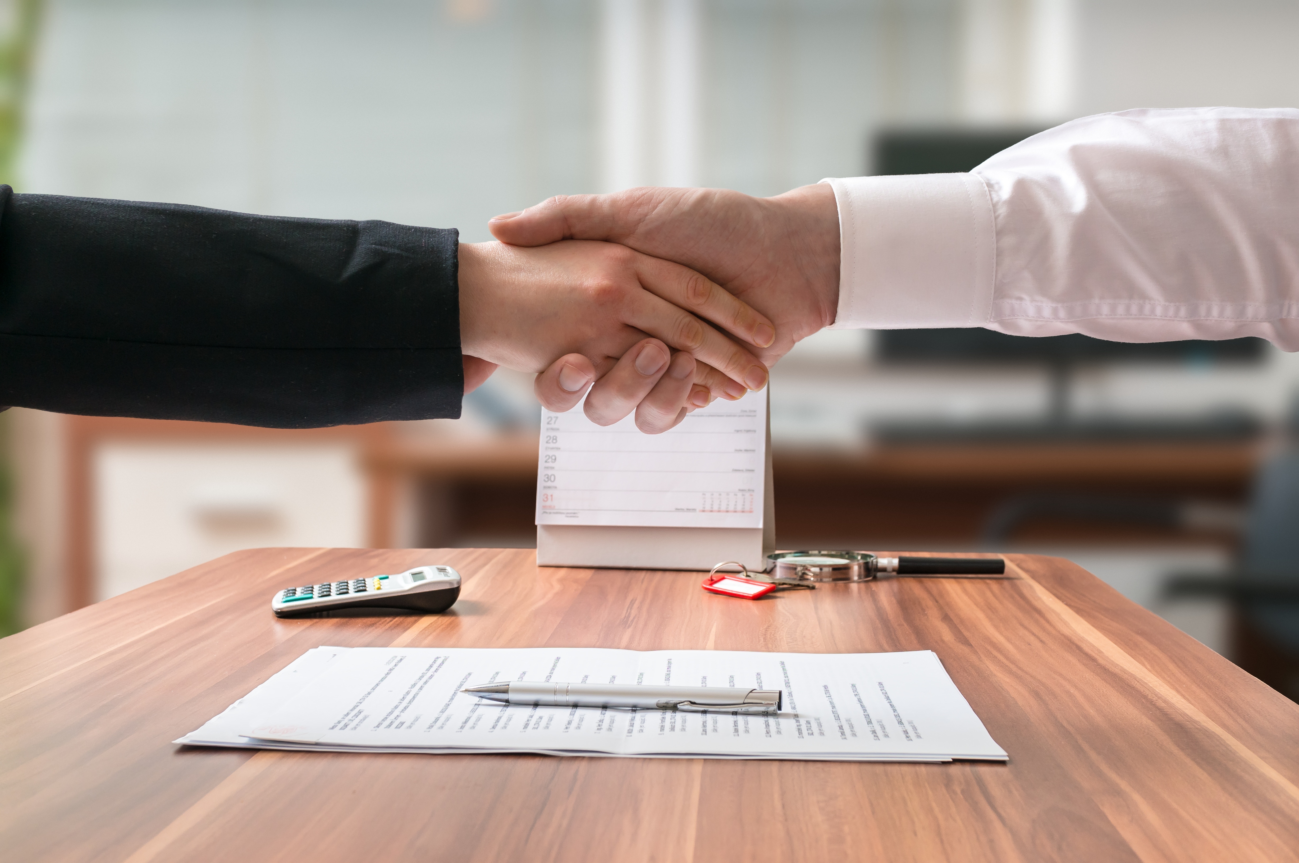 Shakehand of lawyer and business woman sitting behind desk with agreement on blurred background.